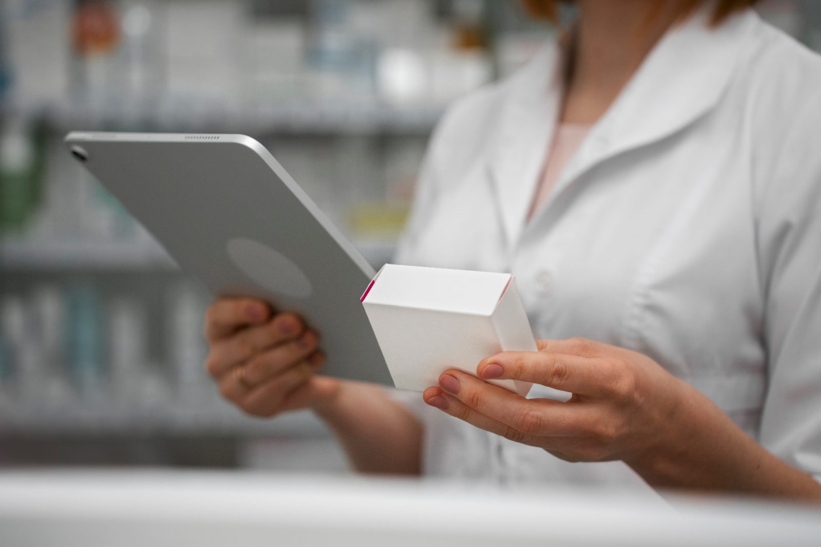 Pozycjonowanie aptek internetowych - farmaceutka w białym fartuchu trzyma tablet i opakowanie leku przy regałach apteki