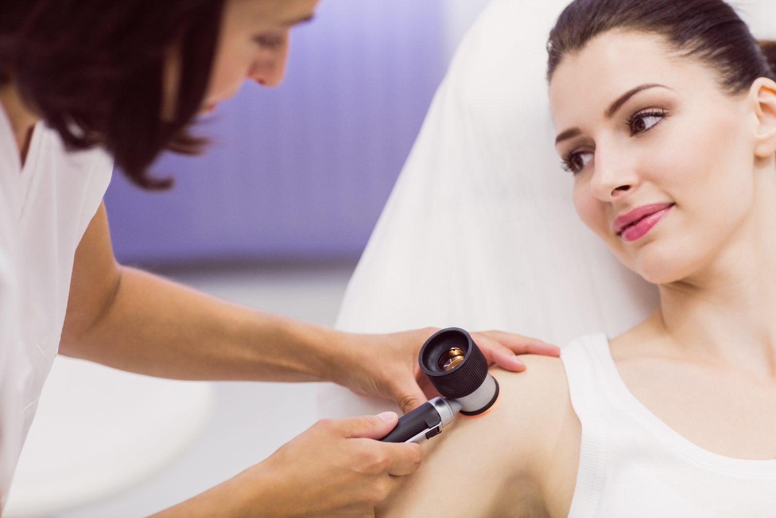 Pozycjonowanie dermatologa - lekarka bada dermatoskopem znamię na ramieniu pacjentki