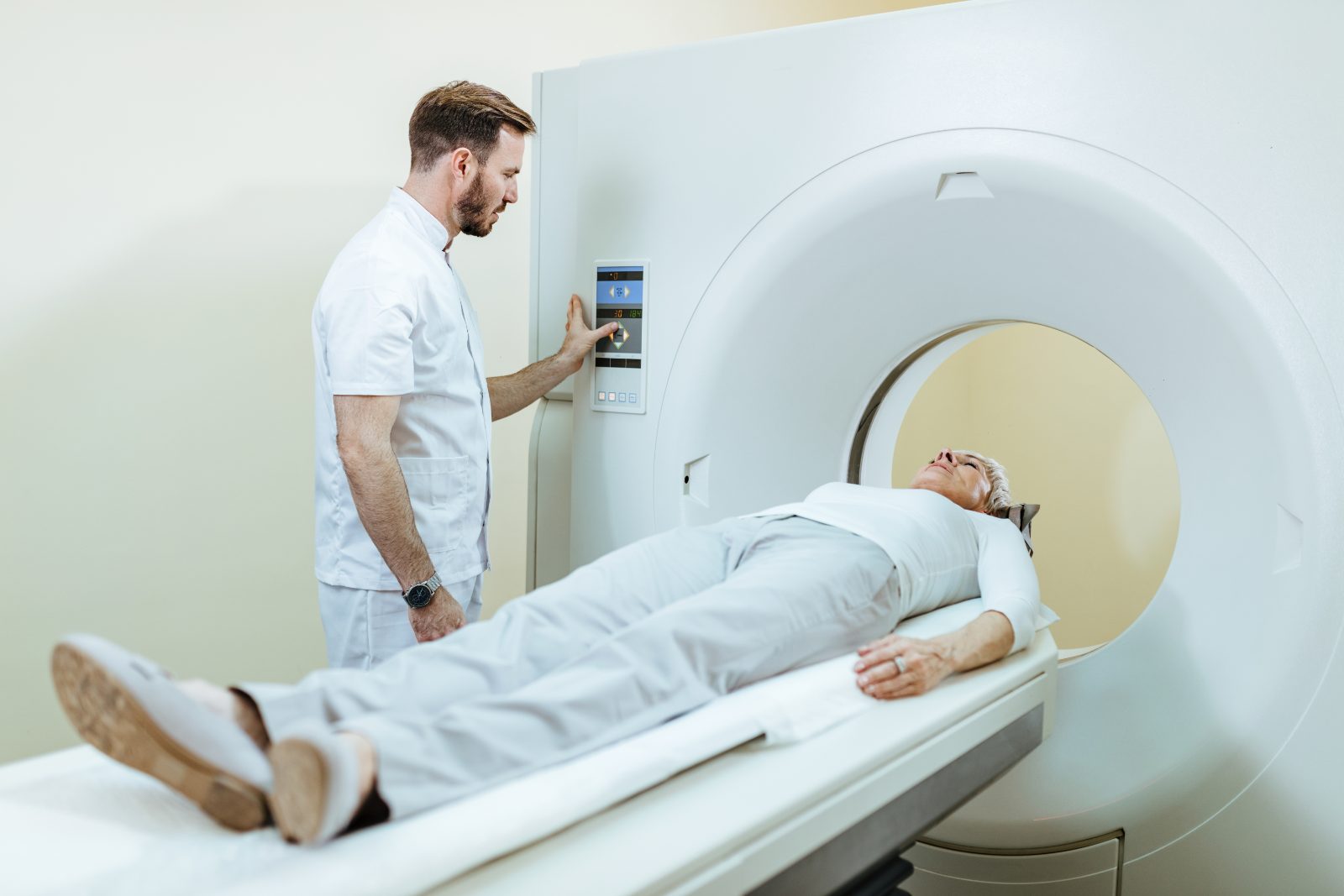 Pozycjonowanie diagnostyki obrazowej - technik obsługuje aparat do badania obrazowego, pacjentka leży na stole przed wjazdem do tunelu