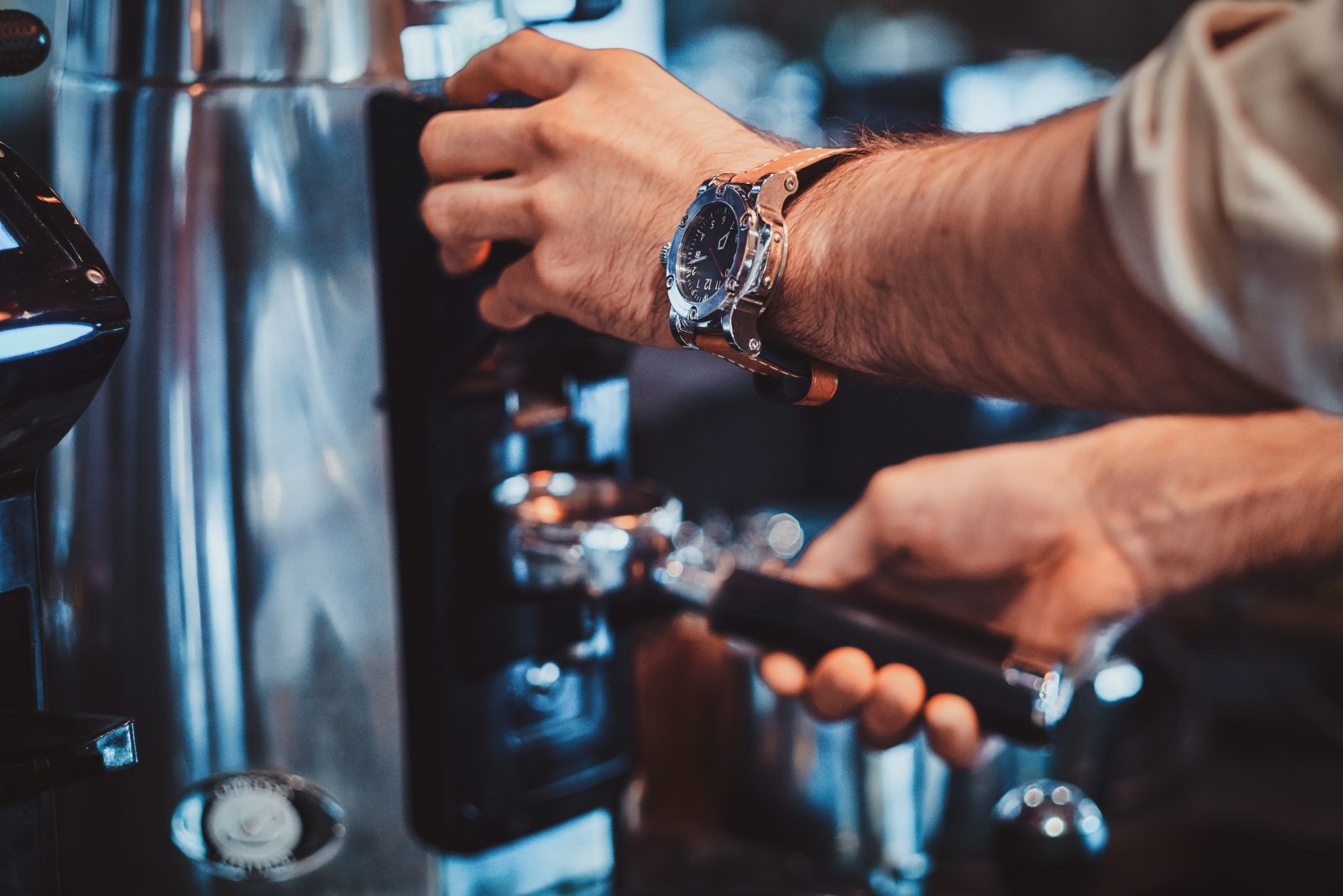 Pozycjonowanie kawiarni - barista wpina kolbę do ekspresu ciśnieniowego, zbliżenie na dłonie