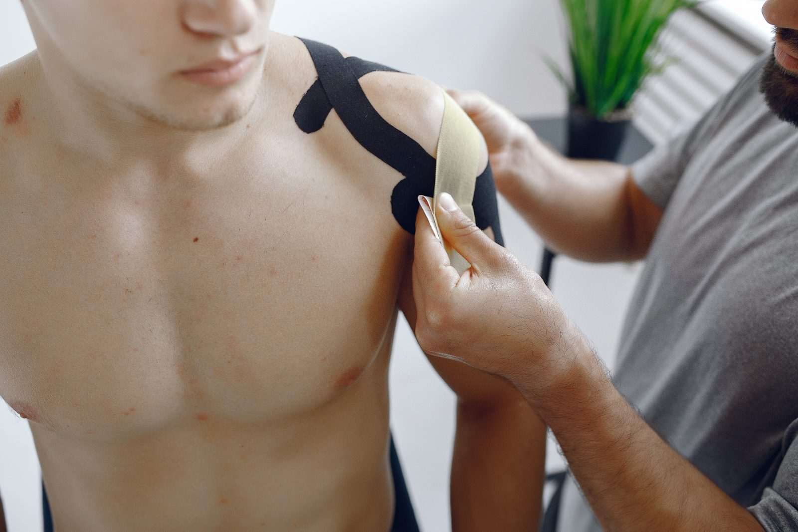 Pozycjonowanie kinesiotapingu - terapeuta nakleja czarną taśmę kinesio na bark pacjenta