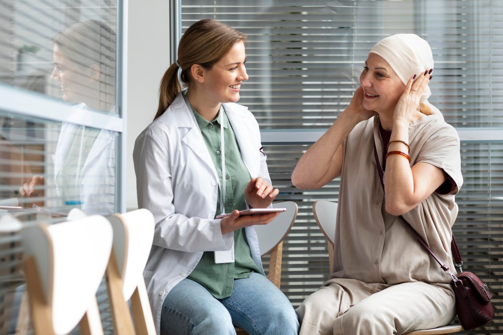 Pozycjonowanie kliniki onkologicznej - uśmiechnięta lekarka z tabletem rozmawia z pacjentką w chuście na głowie w poczekalni