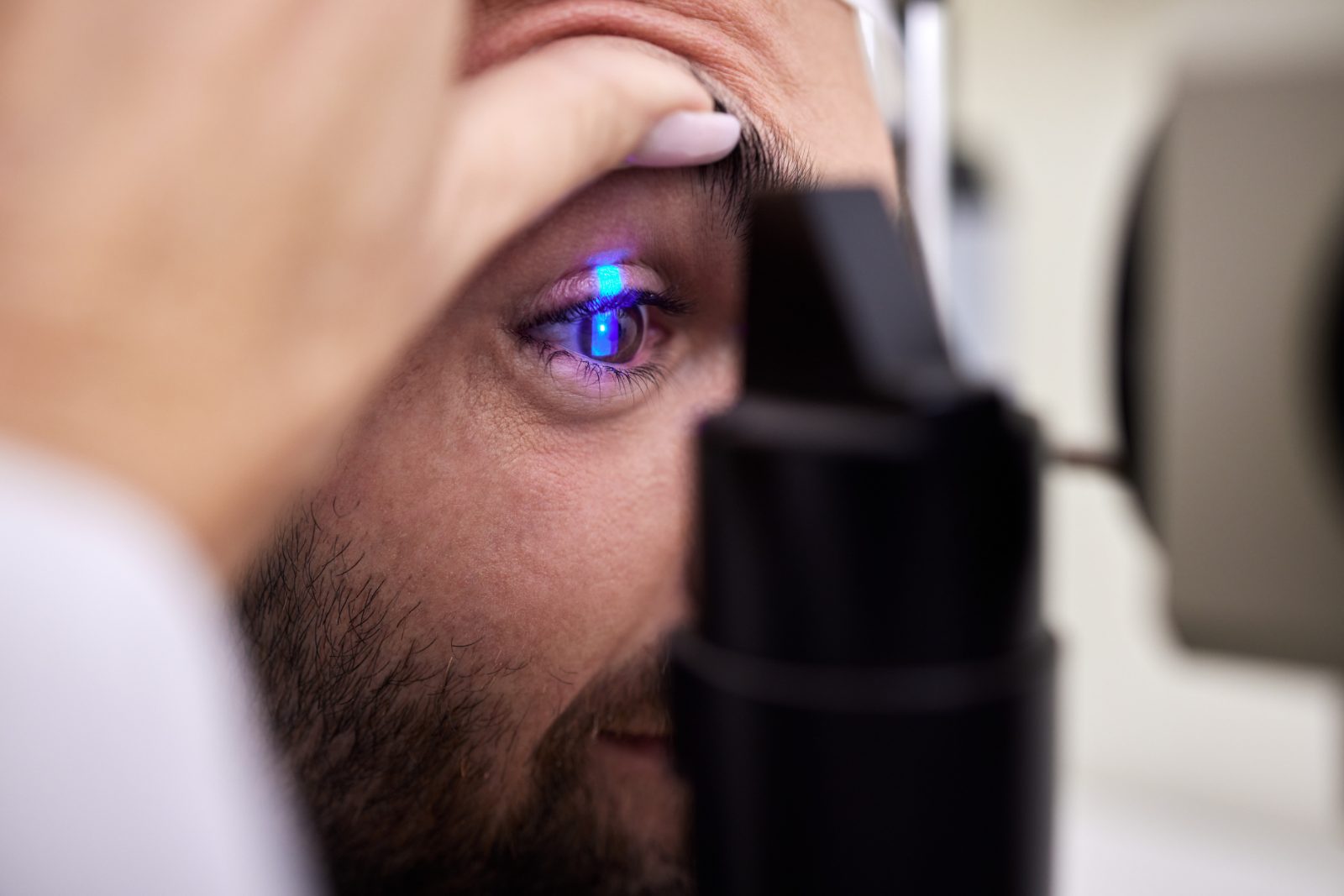 Pozycjonowanie laserowej korekcji wzroku - zbliżenie oka mężczyzny w niebieskim świetle urządzenia, lekarz przytrzymuje powiekę