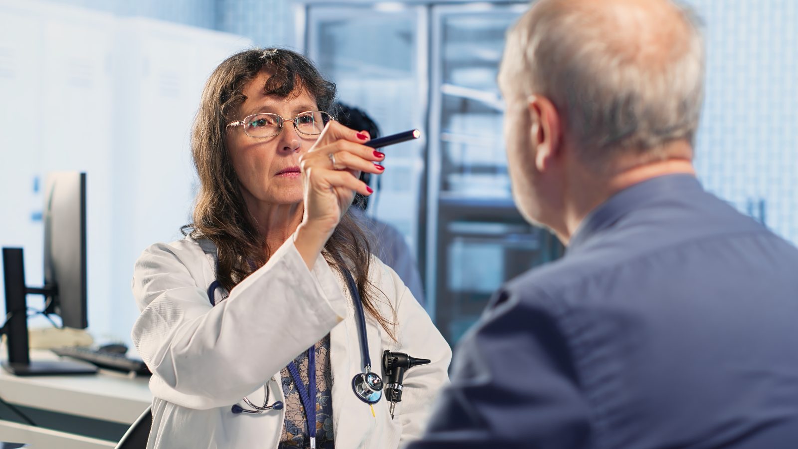 Pozycjonowanie medycyny pracy - lekarka sprawdza latarką diagnostyczną reakcję źrenic pacjenta podczas badania