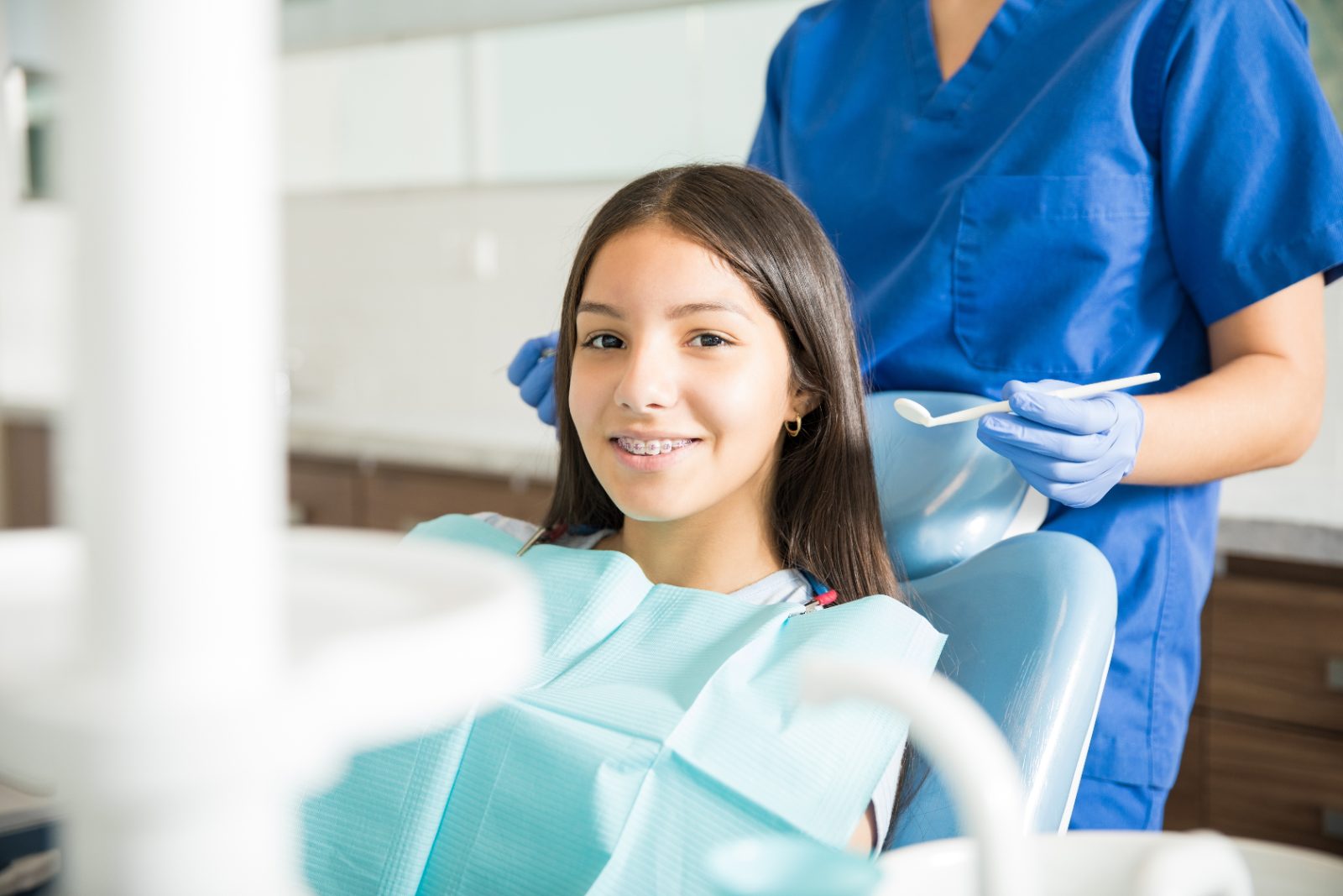 Pozycjonowanie ortodonty - uśmiechnięta nastolatka z aparatem ortodontycznym na fotelu dentystycznym