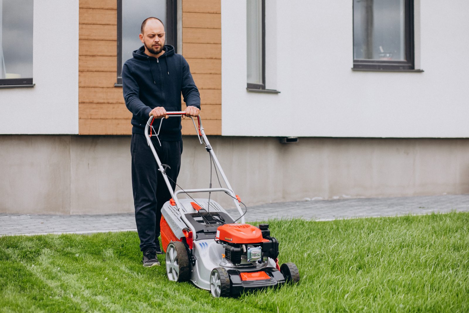 Pozycjonowanie pielęgnacji ogrodów - mężczyzna kosi trawnik spalinową kosiarką przed nowoczesnym domem