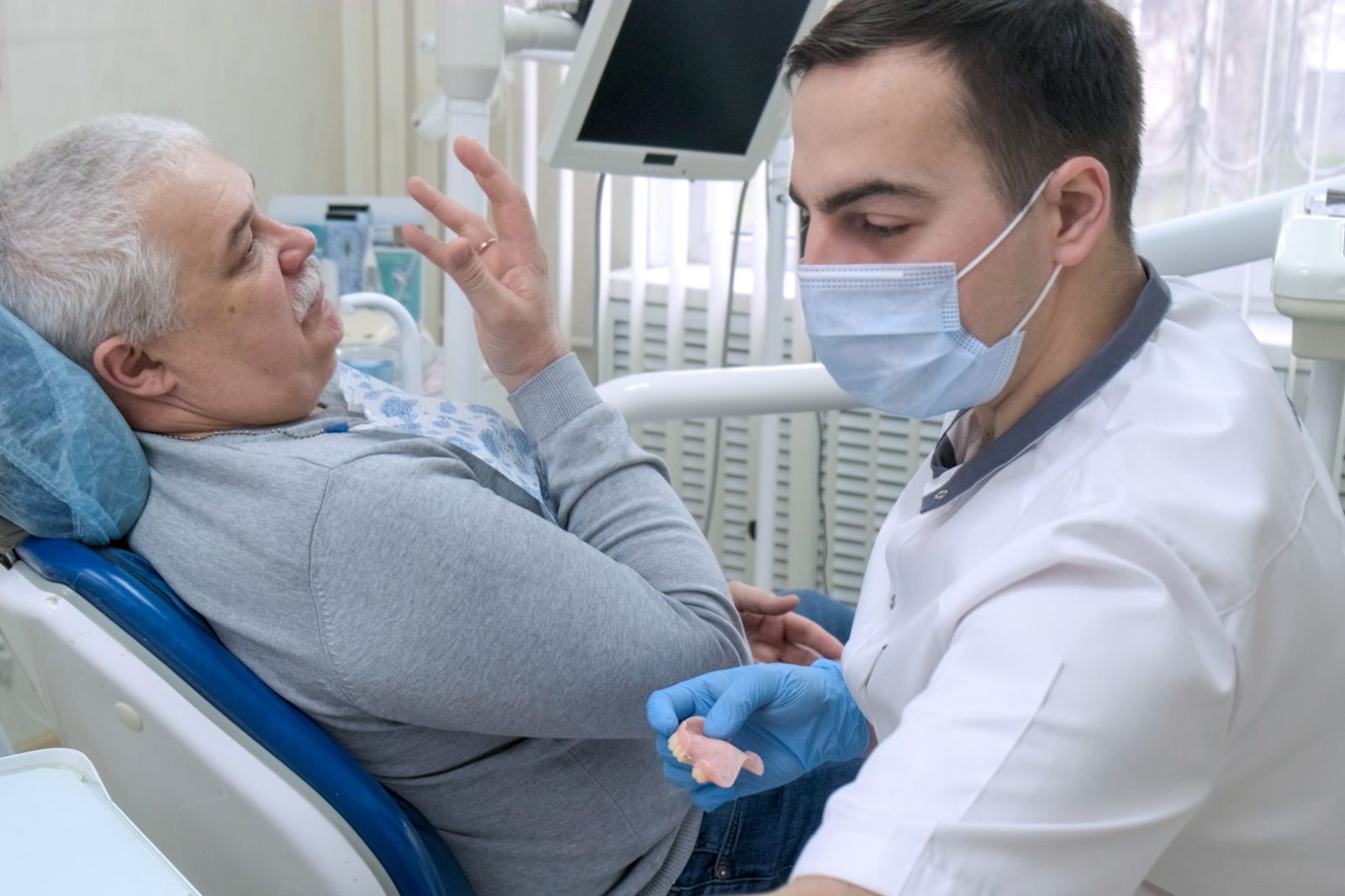 Pozycjonowanie protetyka - dentysta pokazuje protezę zębową starszemu pacjentowi w gabinecie