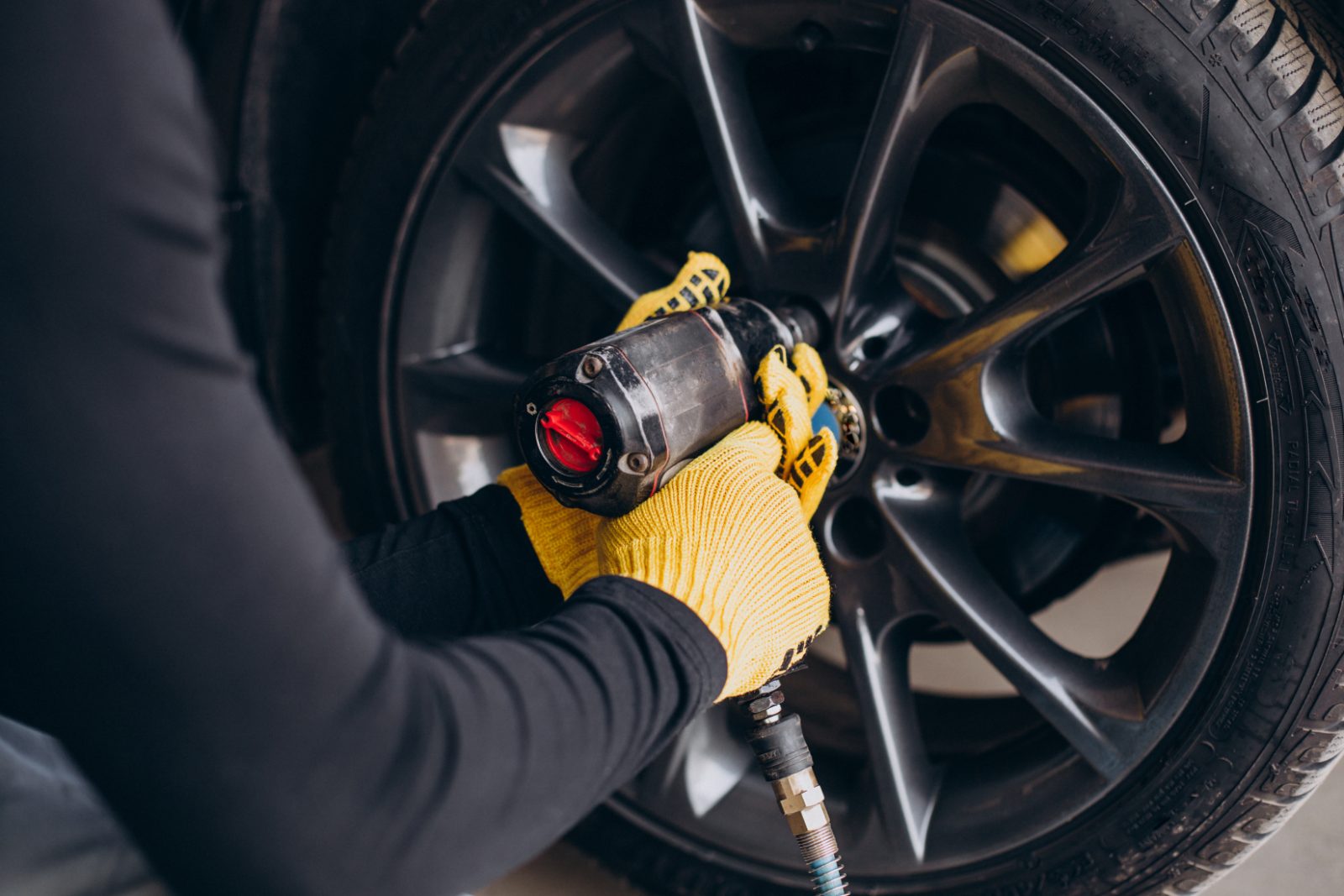 Pozycjonowanie wulkanizacji - mechanik w żółtych rękawicach odkręca koło samochodu kluczem pneumatycznym